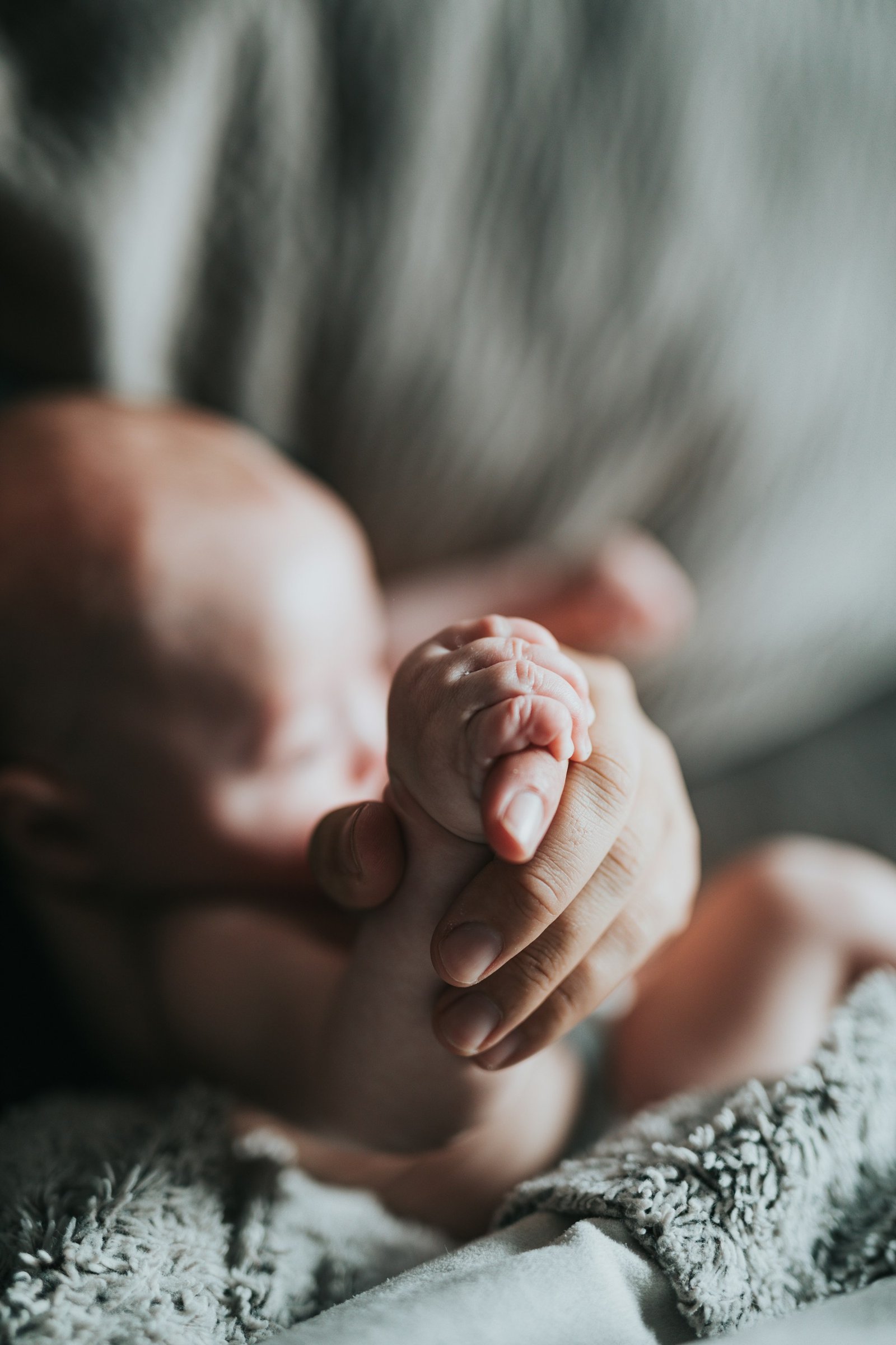 A newborn's small hand wrapped around an adult finger