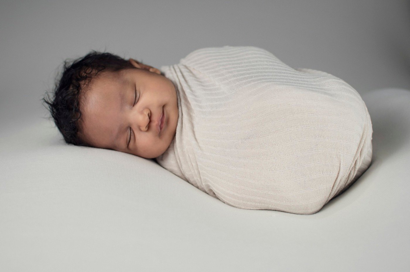 Sleeping newborn wrapped in cream fabric